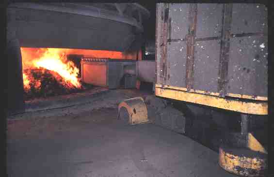 Chargement d'un four de réduction de minerai de chrome. Le minerai et les ferrailles sont chargées par la machine de droite ; on voit brûler les gaz réducteurs inutilisés en surface de la charge. [Ugine S.A.], cliquez pour agrandir